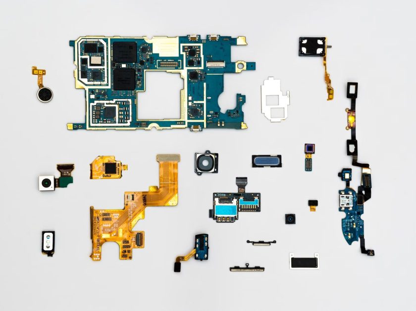 Disassembled smartphone components arranged on a white background. Smartphone electronics spread out to show the motherboard, camera units, and smaller components