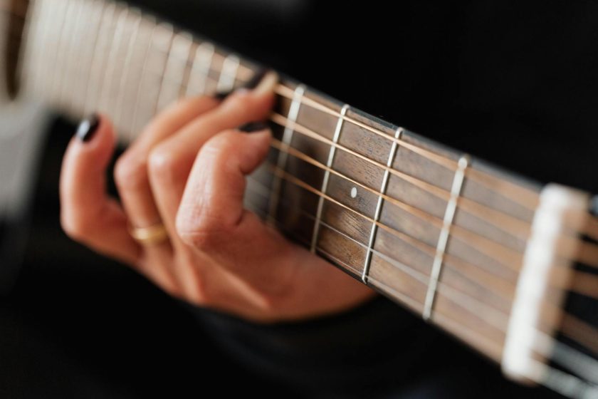 Close-up of hands with black nail polish playing acoustic guitar.